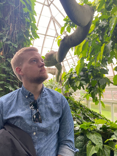 Matt T in a blue shirt standing in front of a tree