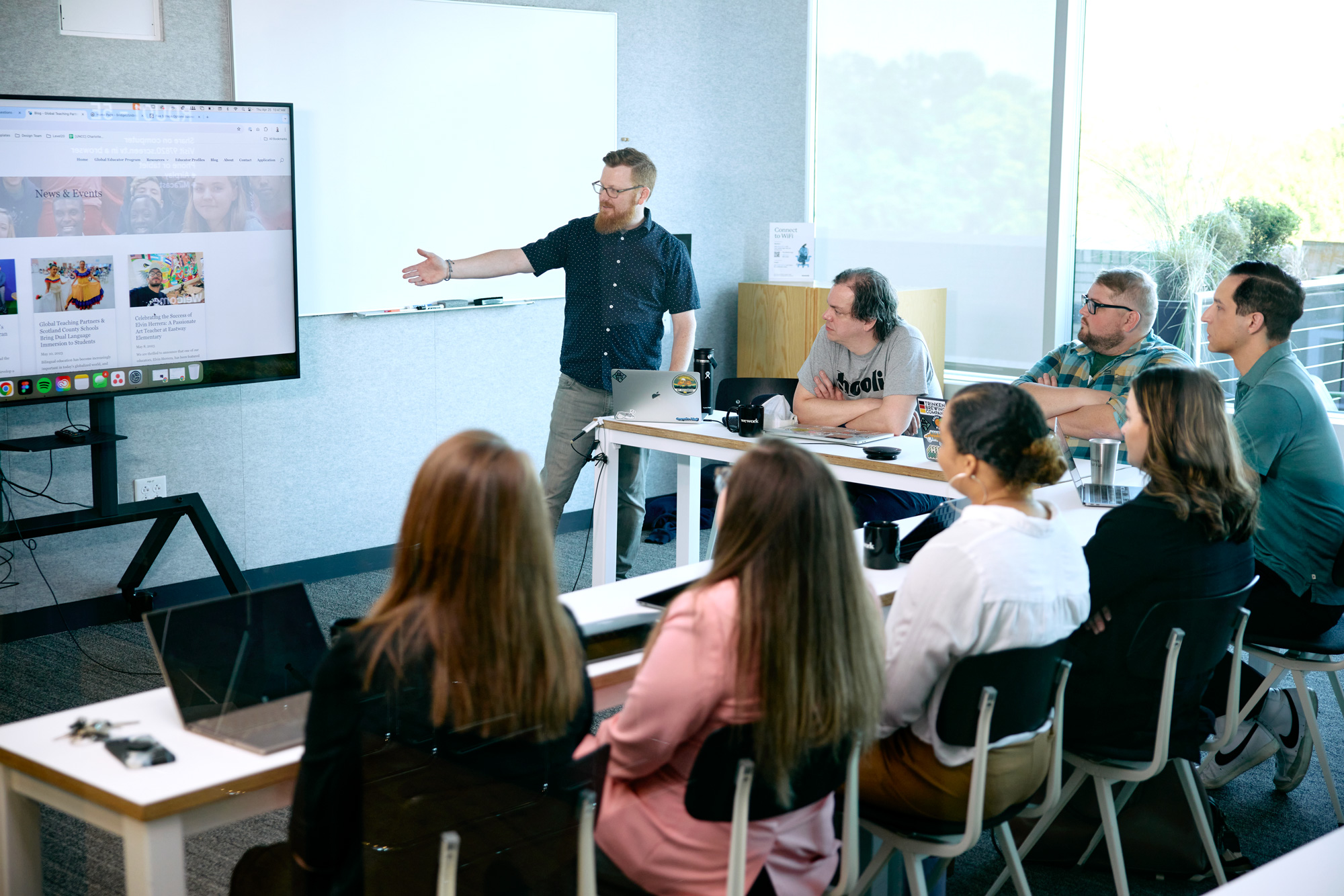 Simon from Savas Labs along side other team members present to a client by pointing to the screen visuals.